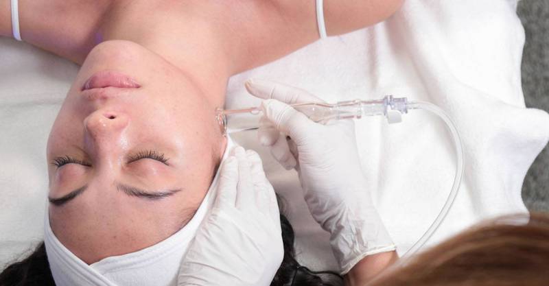 Top view on a relaxed female patient lying on a spa bed. Middle shot on her shoulders and face. A Hydrafacial provider is gently uncovering a new layer of skin with gentle exfoliation and relaxing resurfacing.